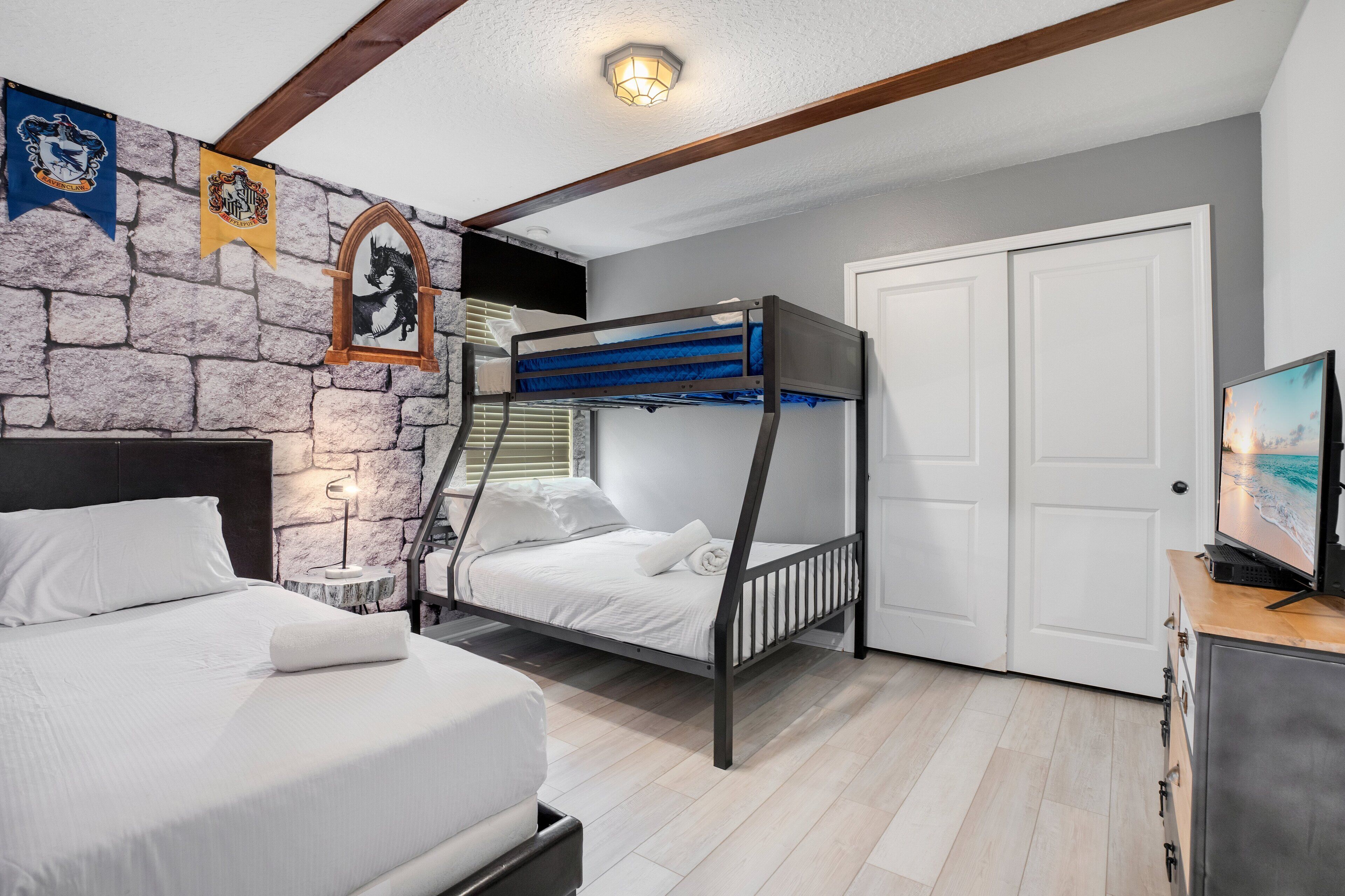 Un dormitorio con una cama litera, una pared de piedra, techo de madera y un televisor sobre un aparador.