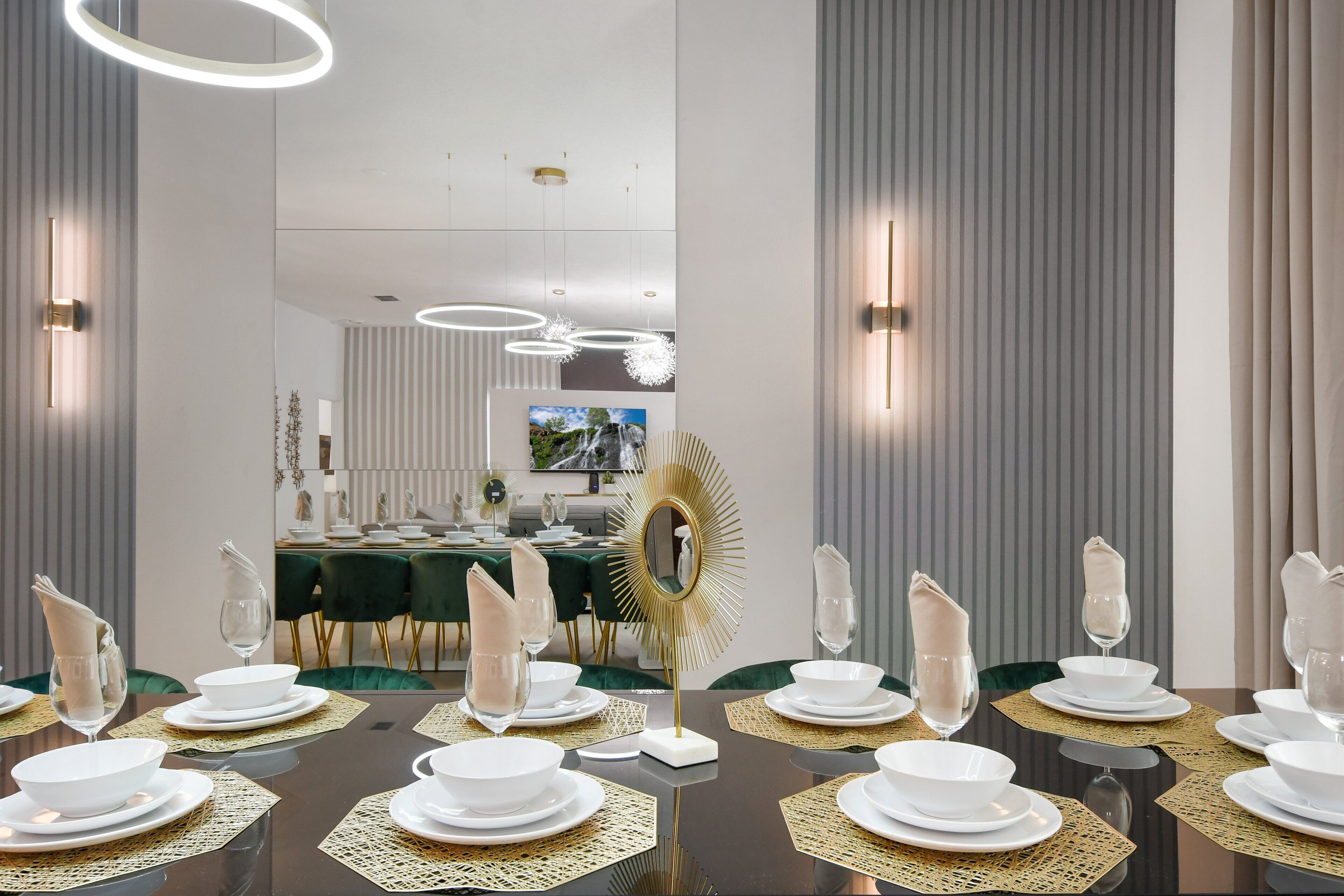 A dining area with a long table set for a meal, featuring gold placemats, white plates, and clear glassware.