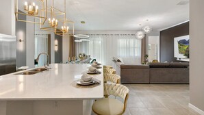 Een moderne keuken met een centraal eiland, hangende lampen en een eethoek met stoelen.