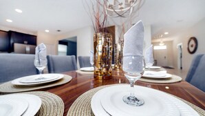 Une table à manger dressée avec de l’assiette blanche, de la verrerie transparente et des sets de table en fibres tressées.