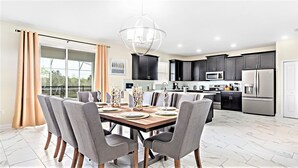 Une cuisine moderne avec des meubles de couleur sombre, des appareils en acier inoxydable et un coin repas comprenant une table en bois et des chaises grises.
