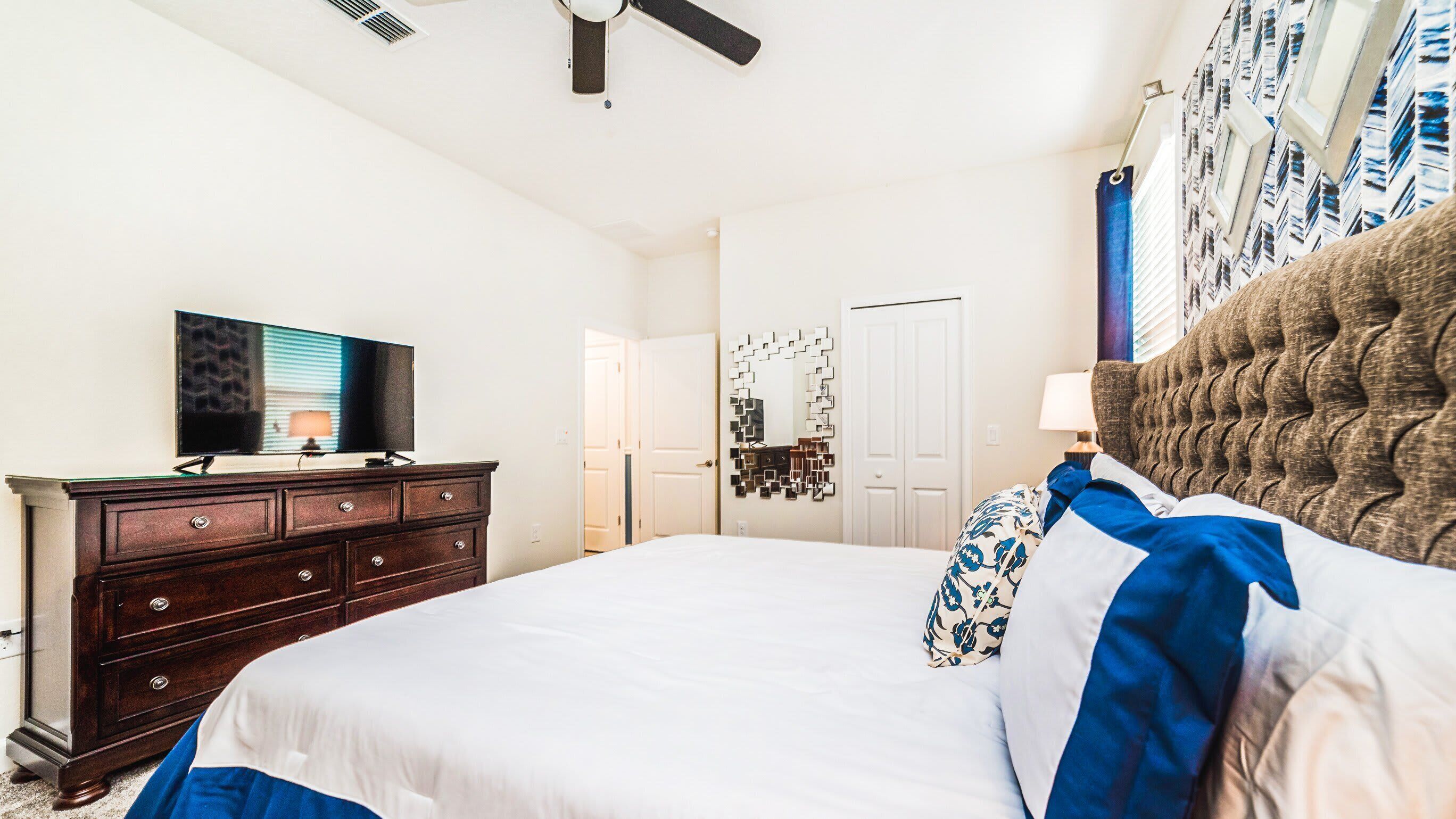 A bedroom with a large bed, a dresser, a television, and a ceiling fan.