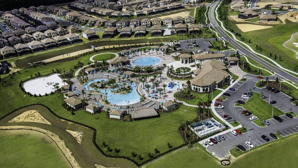 Vista aérea de un resort con múltiples piscinas, un campo de golf y un estacionamiento.