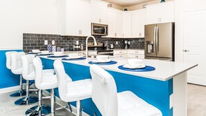 Una cocina moderna con gabinetes blancos, salpicadero de azulejos negros, electrodomésticos de acero inoxidable y una pared de acento azul.