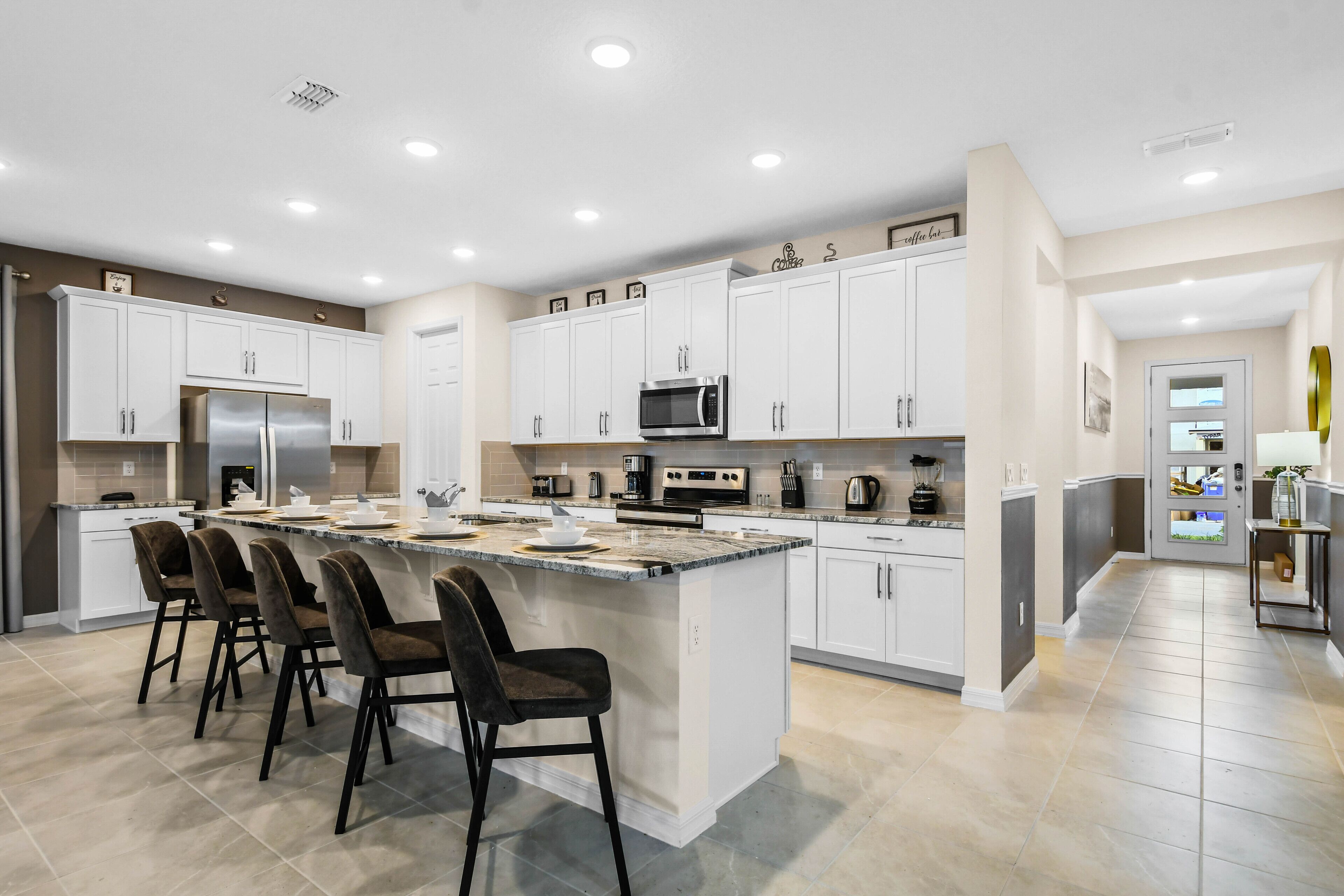 A modern kitchen with white cabinets, a large island with bar stools, and a stainless steel refrigerator.