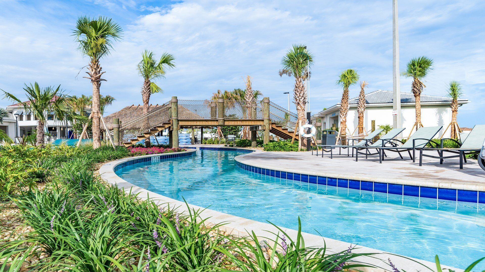 A swimming pool with palm trees, lounge chairs, and a covered area.