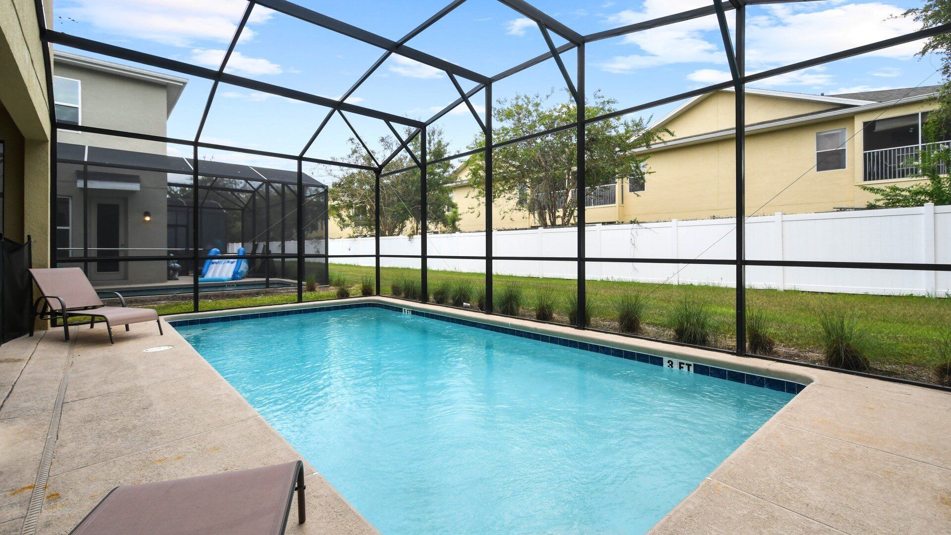 A swimming pool with a glass enclosure, a lounge chair, and a view of neighboring houses.