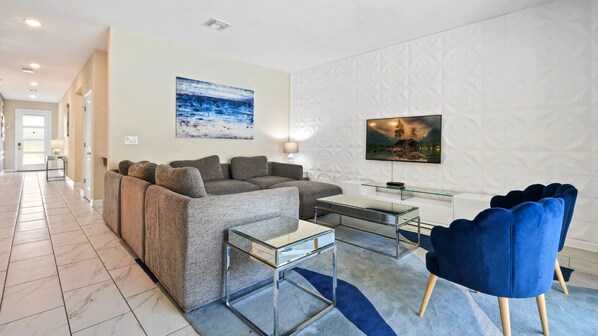 A modern living room with a sectional sofa, a glass coffee table, and a blue armchair.