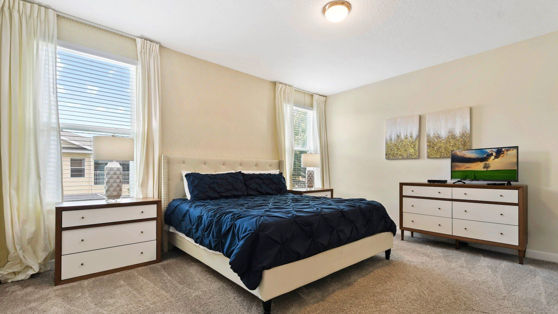 A bedroom with a bed, two nightstands, a dresser, a TV, and artwork on the wall.