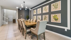 A dining area with a long wooden table, six upholstered chairs, and a modern chandelier. - Comfort & Luxury Near Orlando Attractions (Davenport)