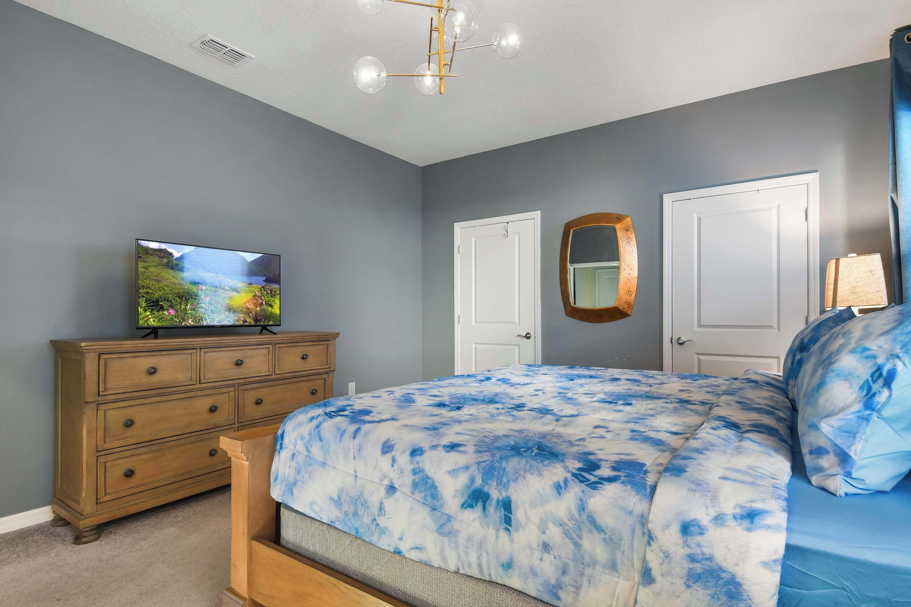 Quarto com cama, penteadeira, televisão e duas portas.