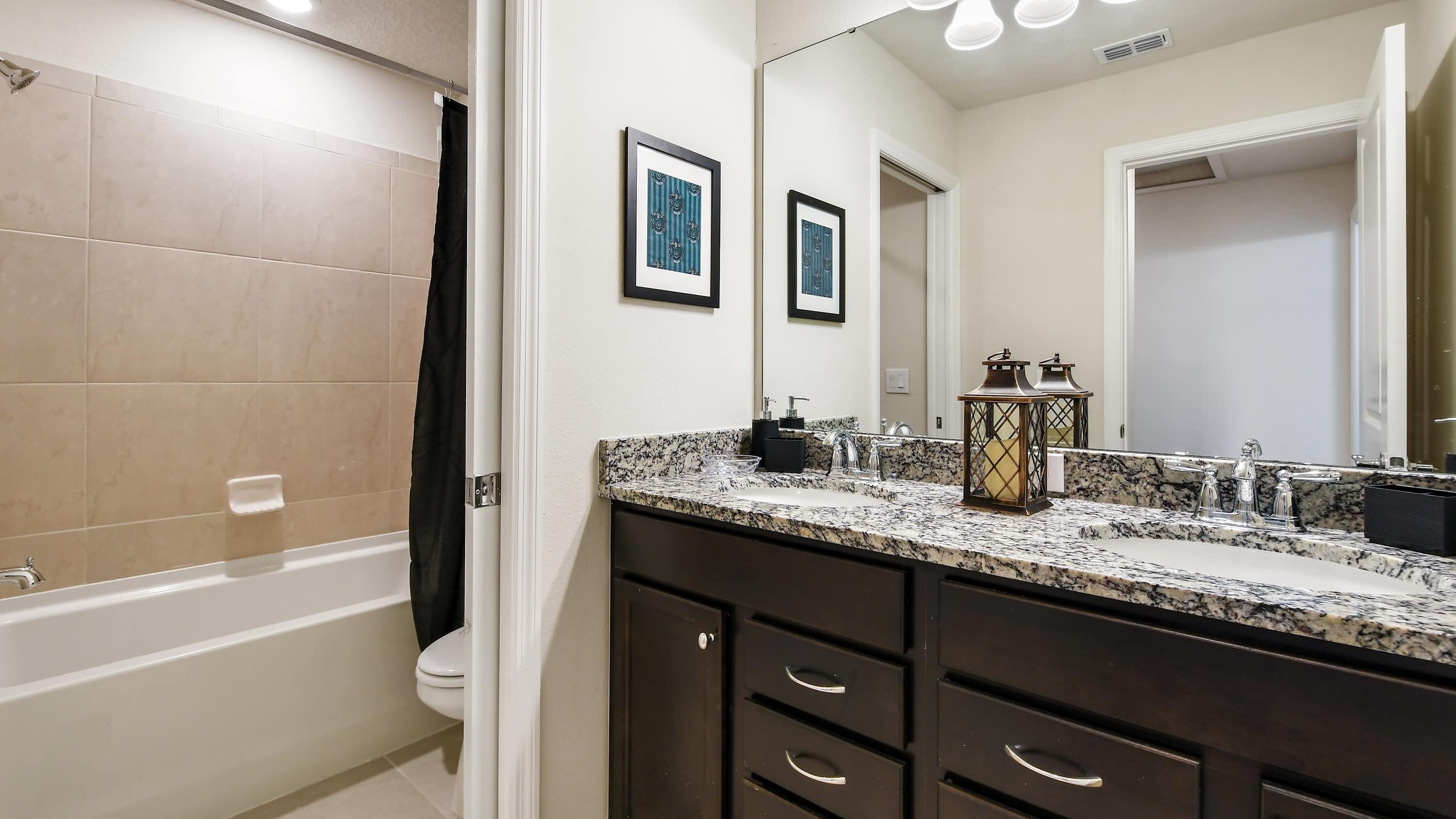 A bathroom with a bathtub, a toilet, a vanity with a sink, and a large mirror.