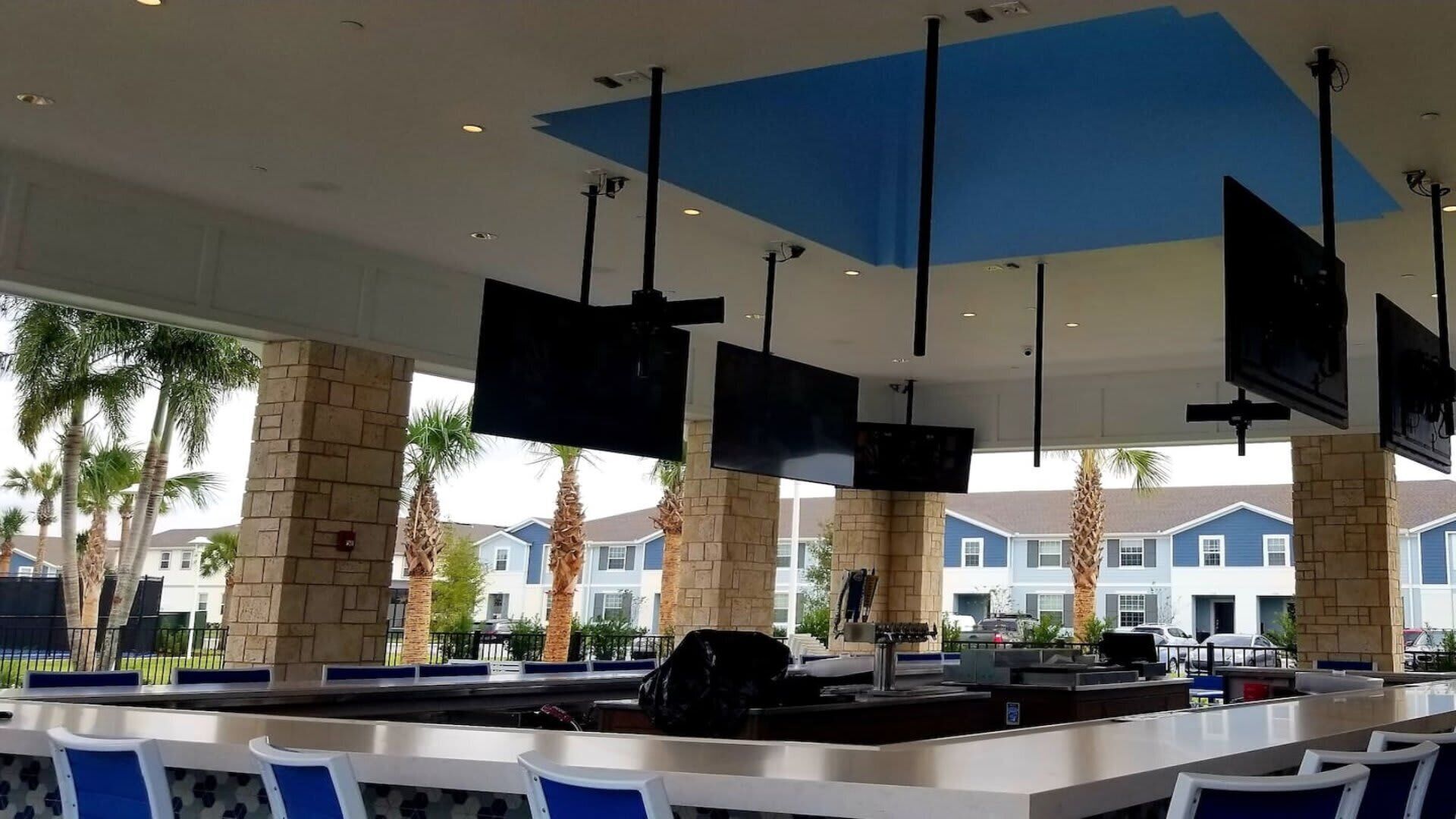 A bar area with multiple screens, seating, and a view of residential buildings.