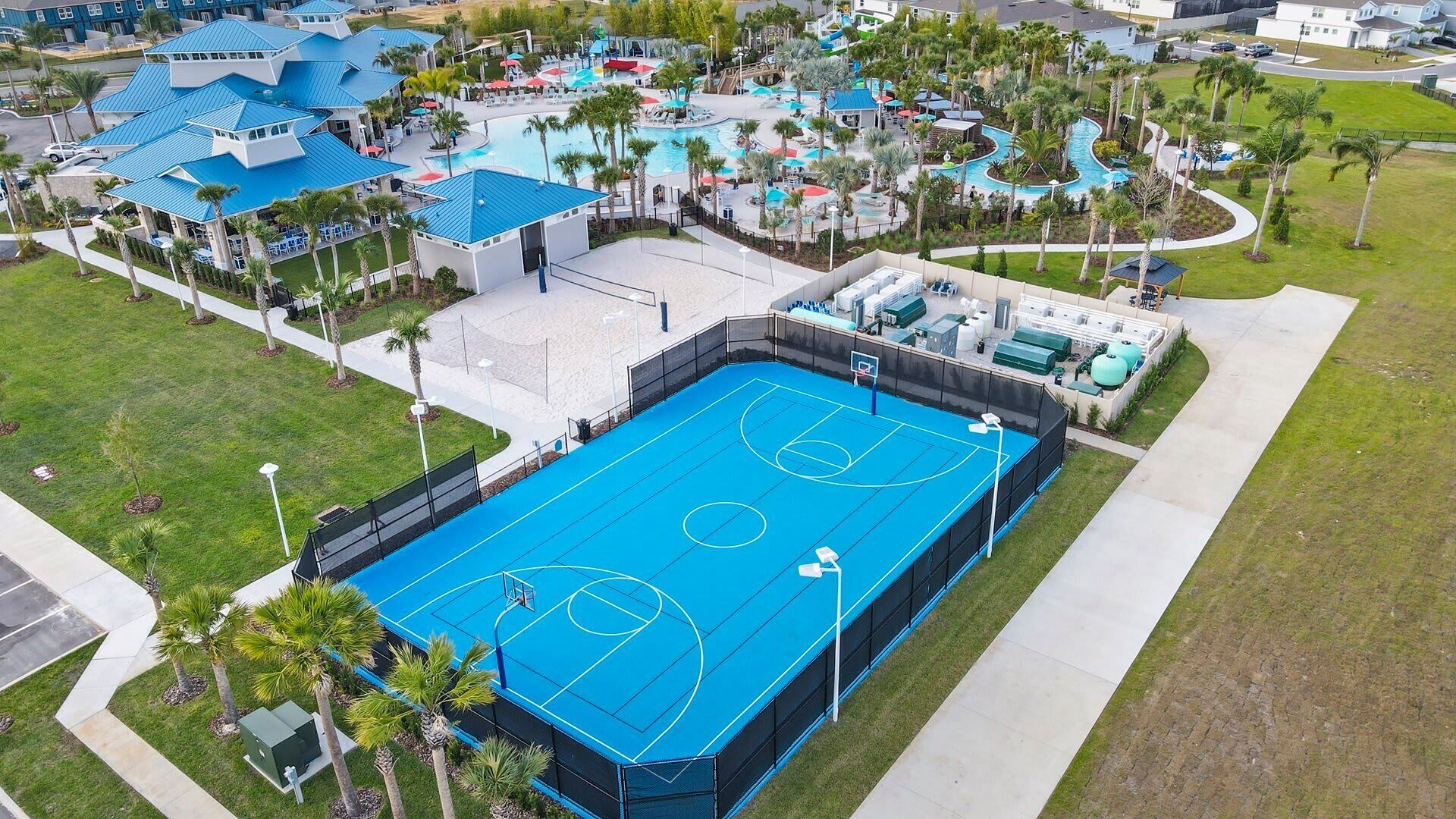 An aerial view of a resort with multiple swimming pools, a basketball court, and surrounding palm trees.