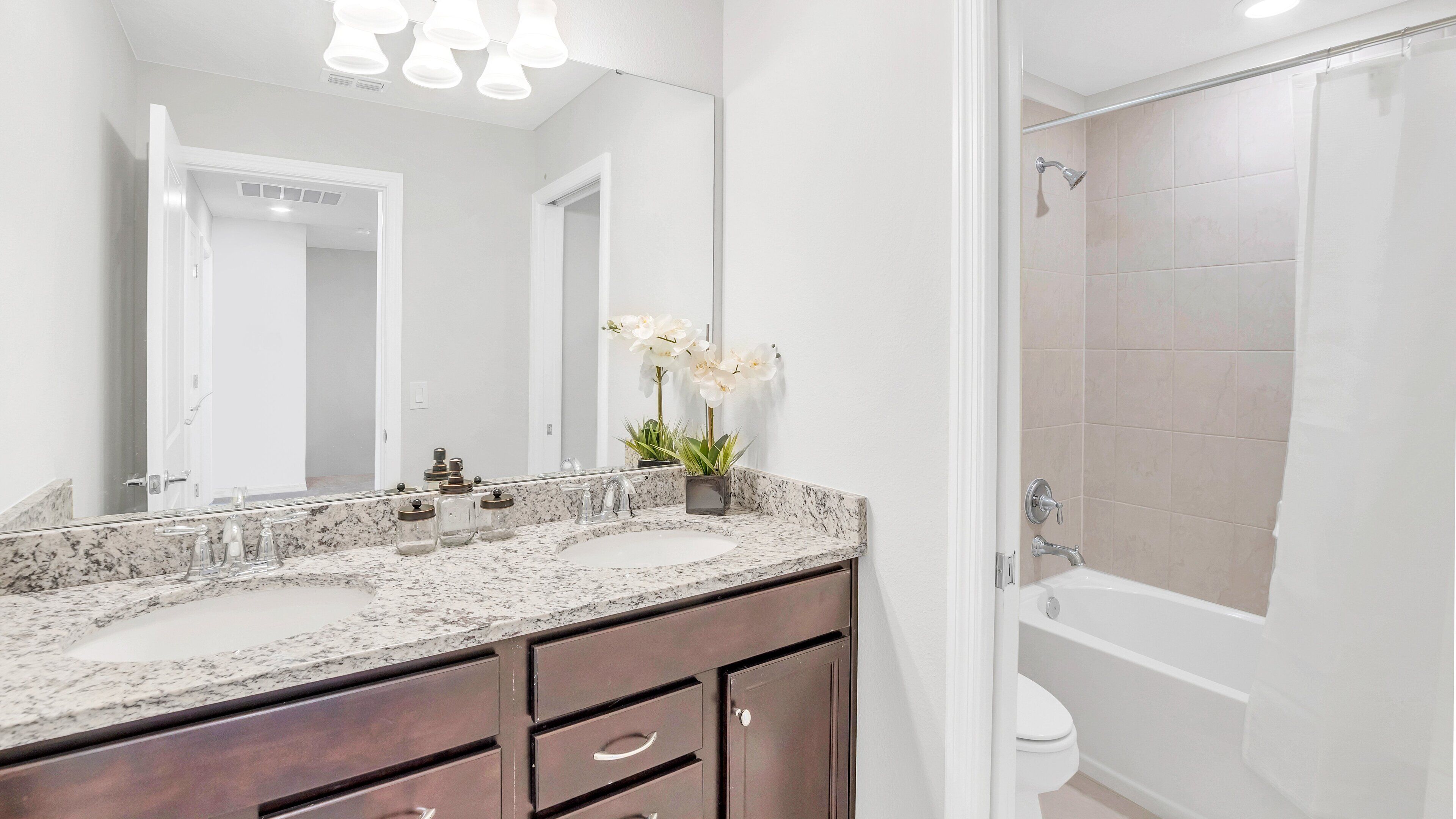 A bathroom with two sinks, a mirror, a shower, and a toilet.
