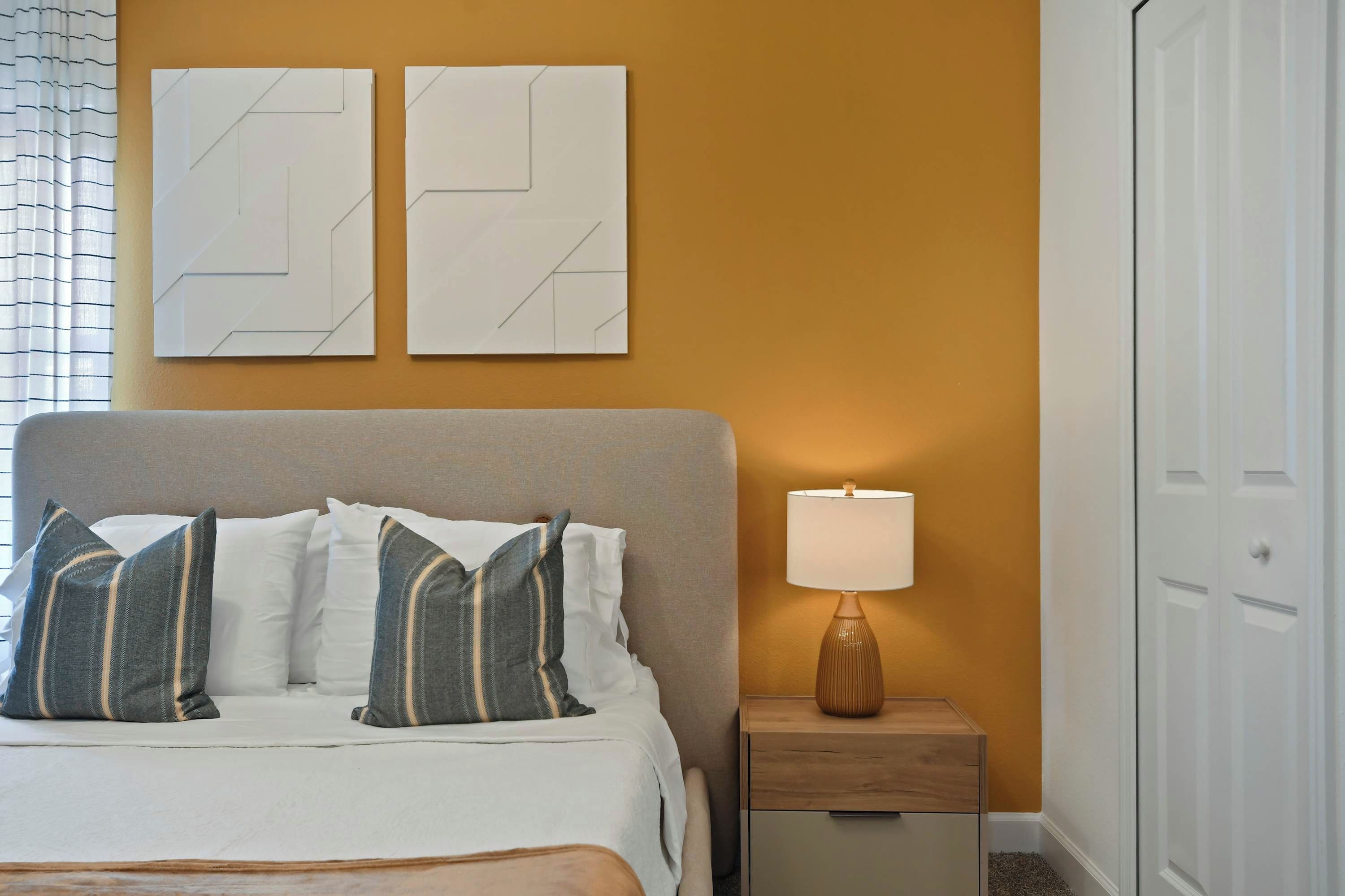 Une chambre à coucher comprenant un lit, des oreillers, une table de chevet, une lampe et deux œuvres d’art murales.