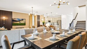 A modern dining room with a long table set for six, a kitchen in the background, and a staircase leading to an upper floor. - Storey Lake Fantastic Star Wars Villa With Lakeview 2913 (Kissimmee)