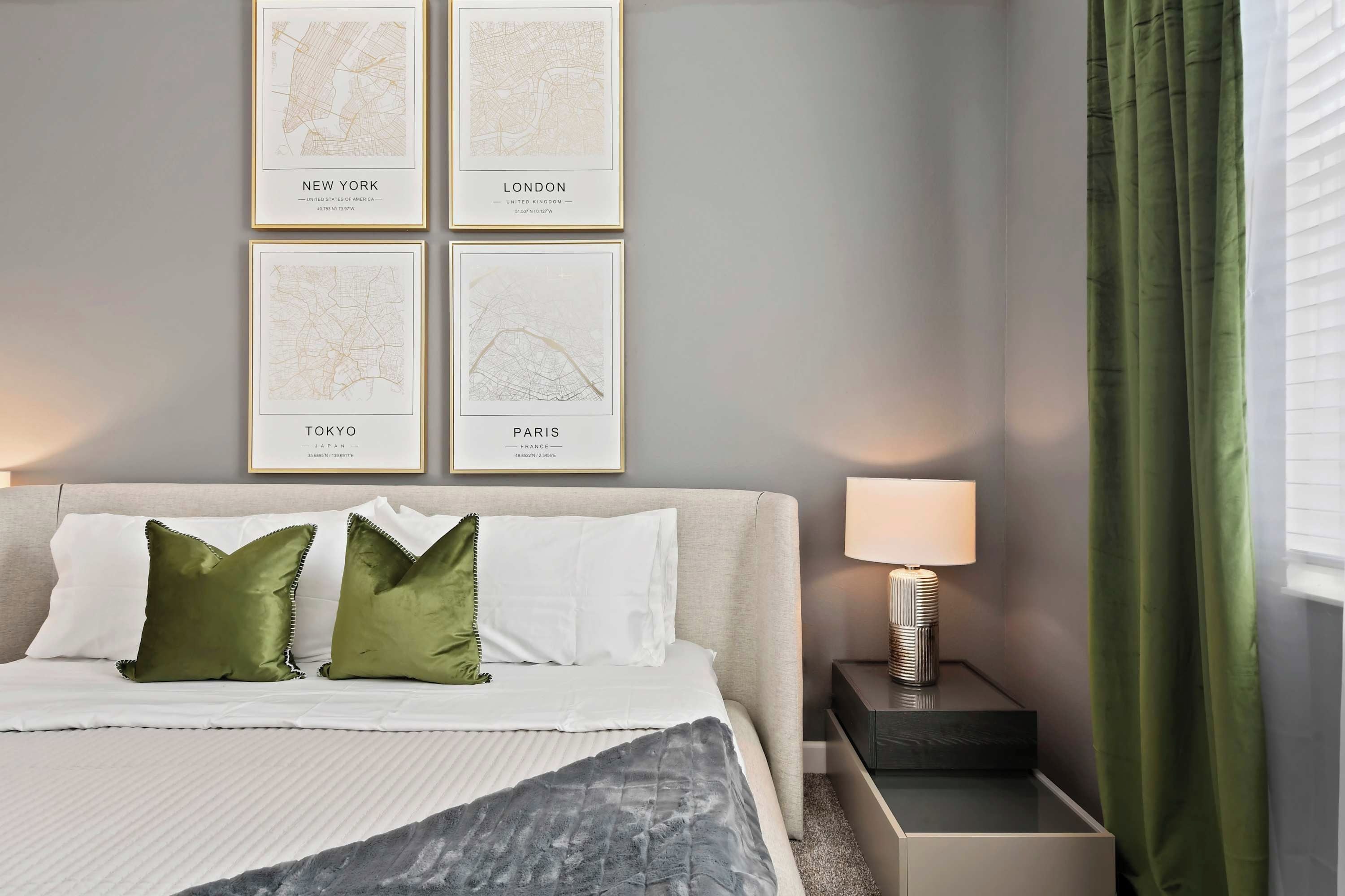 Une chambre d’hôtel bien rangée, avec un lit, des oreillers, une table de chevet, une lampe et une fenêtre avec des rideaux.