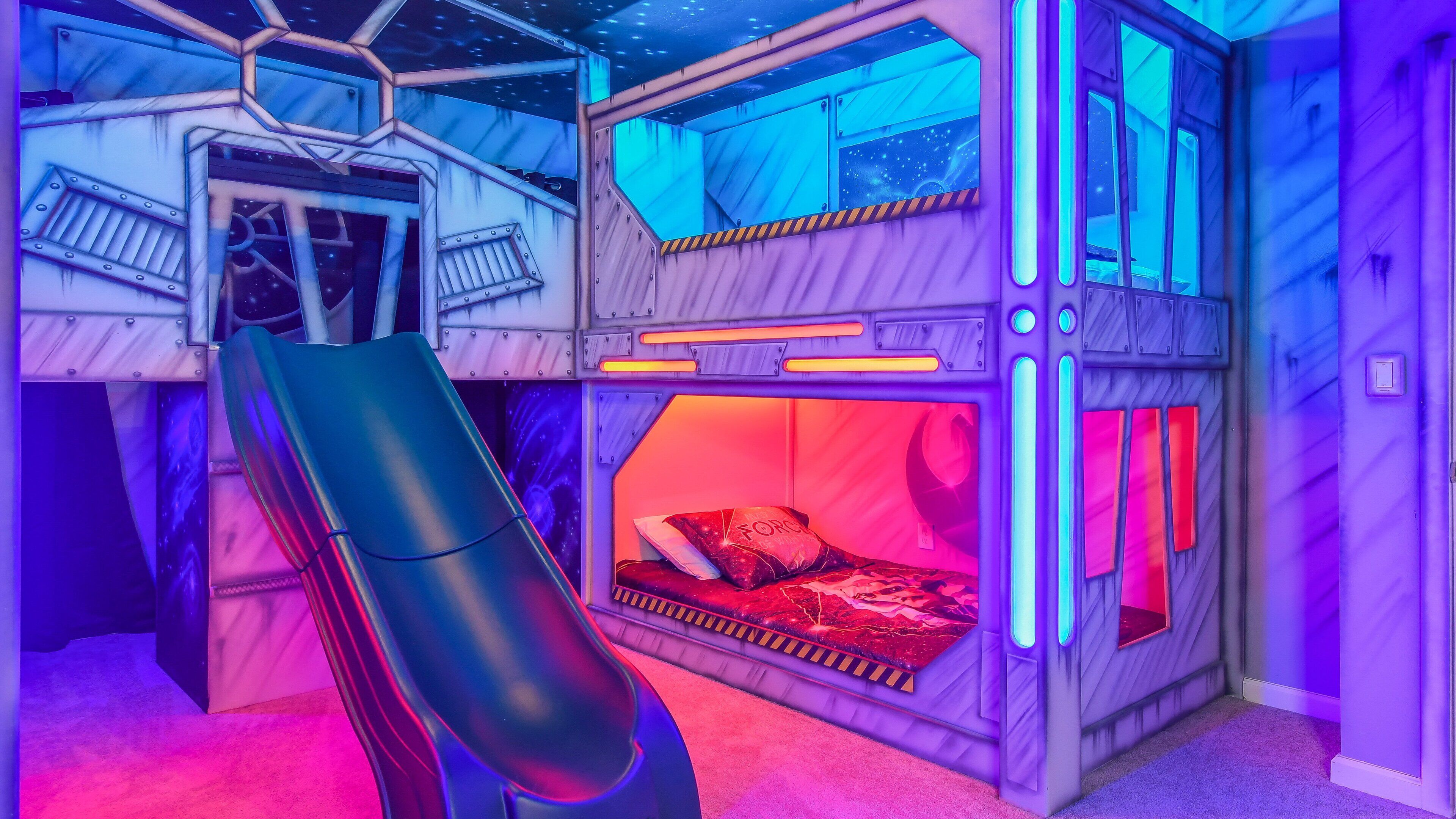 A bunk bed room with a slide, starry ceiling, and neon lights.