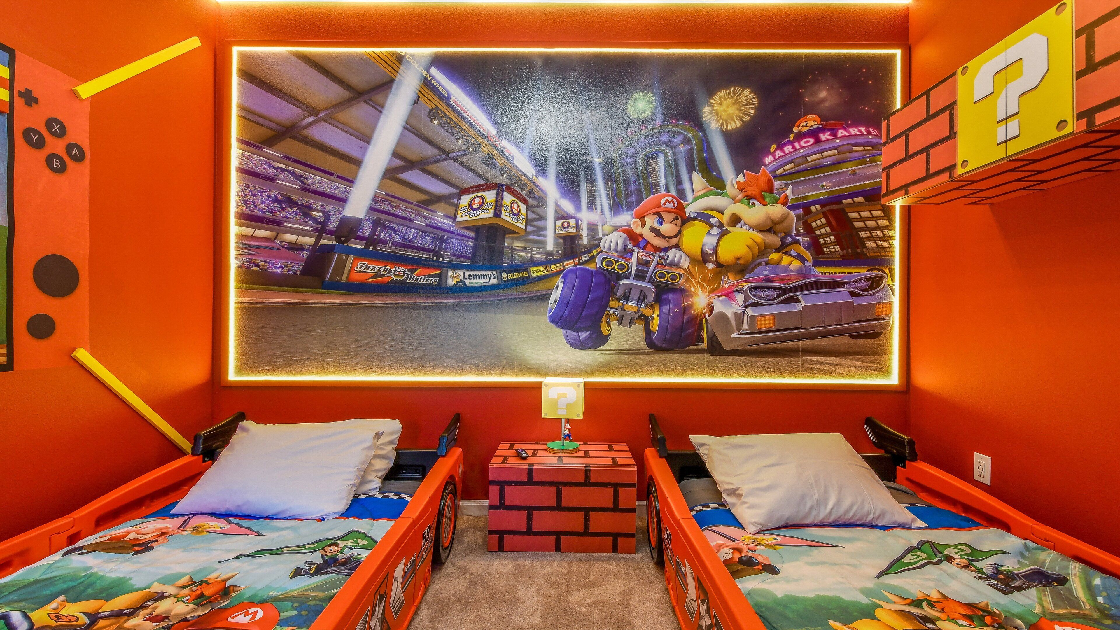 A room with two beds, a large wall mural of Mario Kart, and a brick-patterned nightstand.