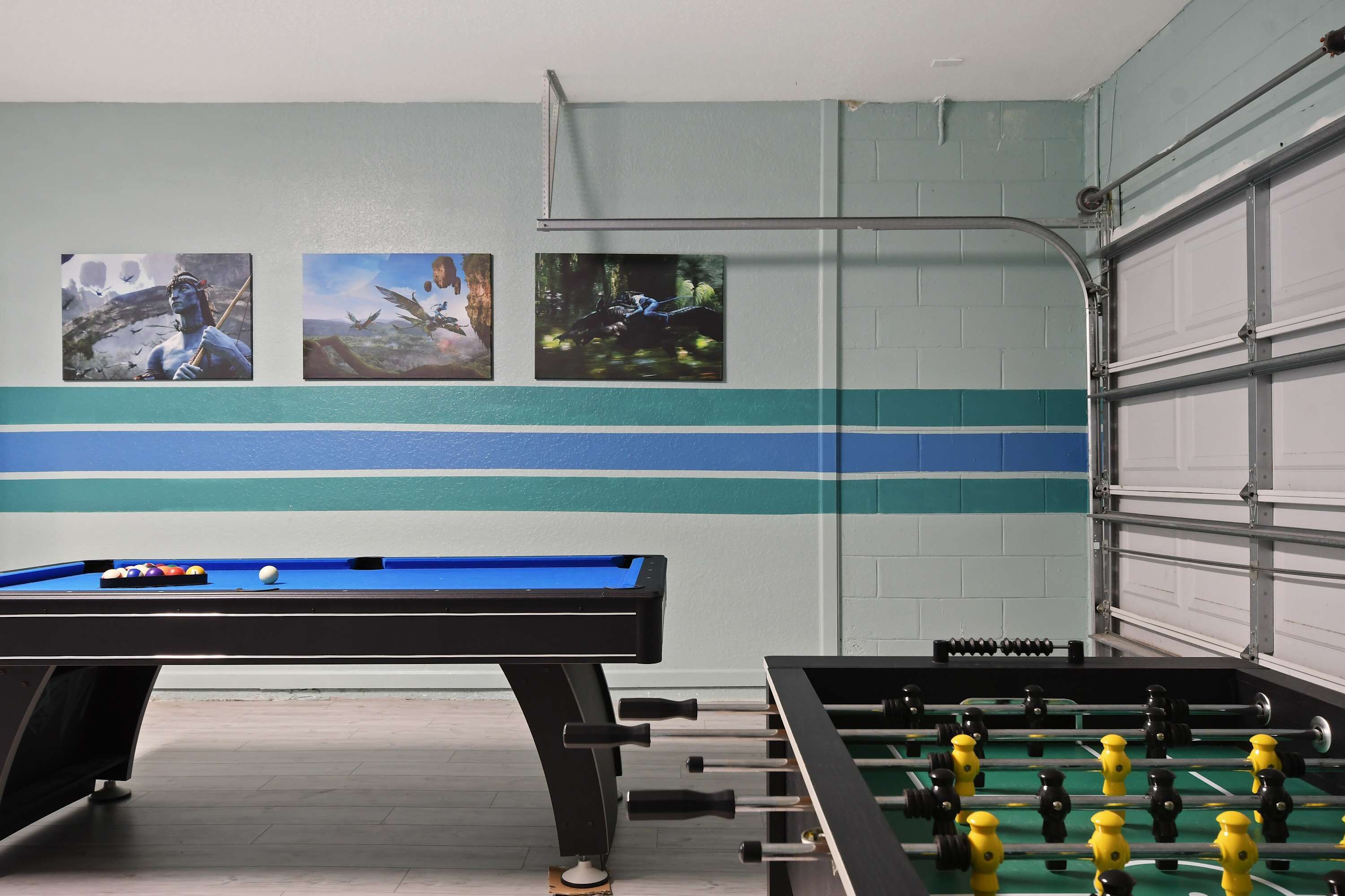 A pool table with a foosball table beside it, and three framed pictures on the wall.