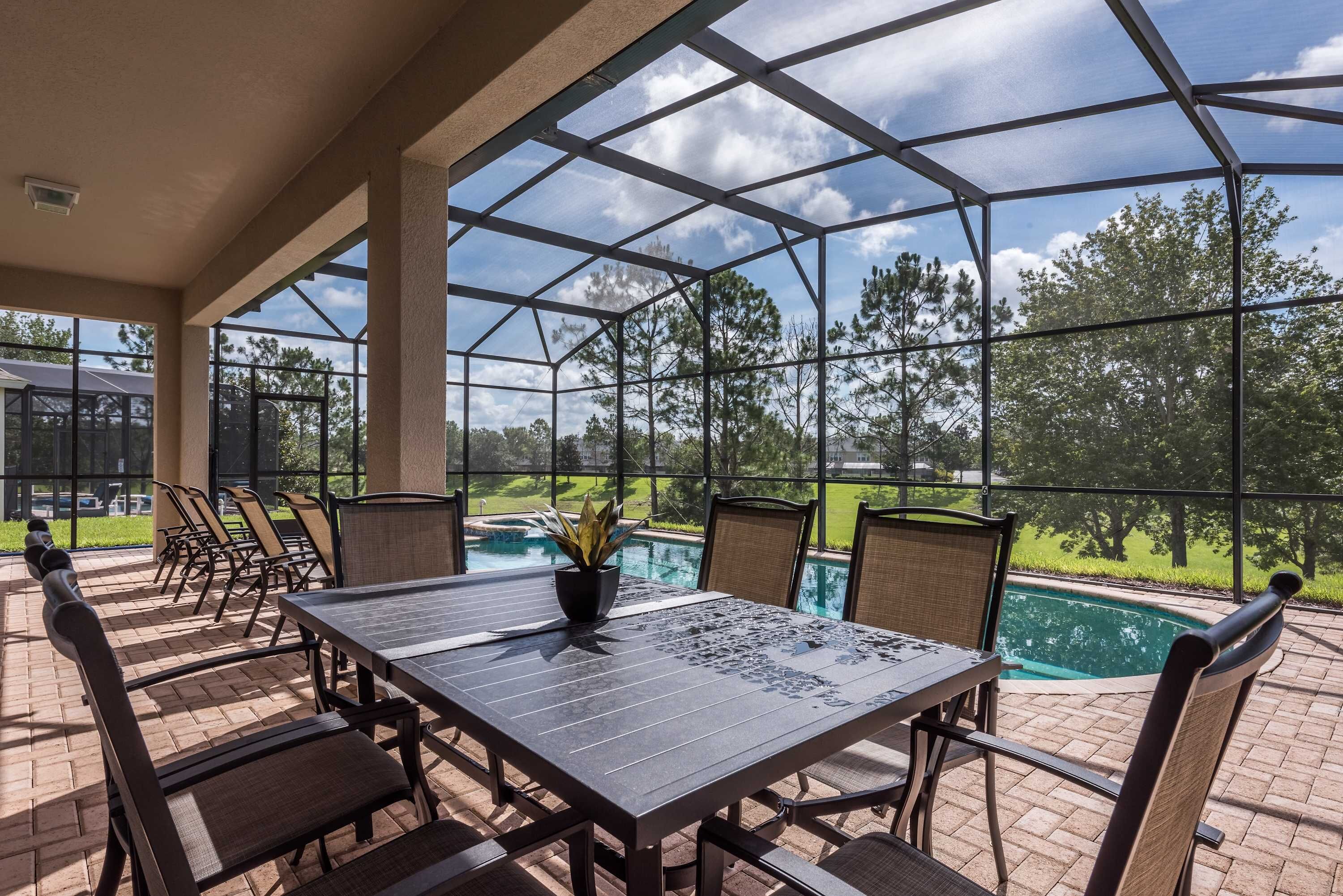 A covered patio area with a table and chairs, overlooking a swimming pool and a landscaped garden.