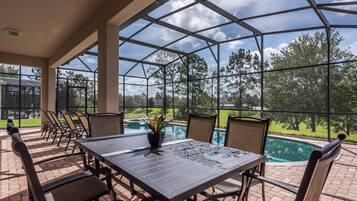 A covered patio area with a table and chairs, overlooking a swimming pool and a landscaped garden.