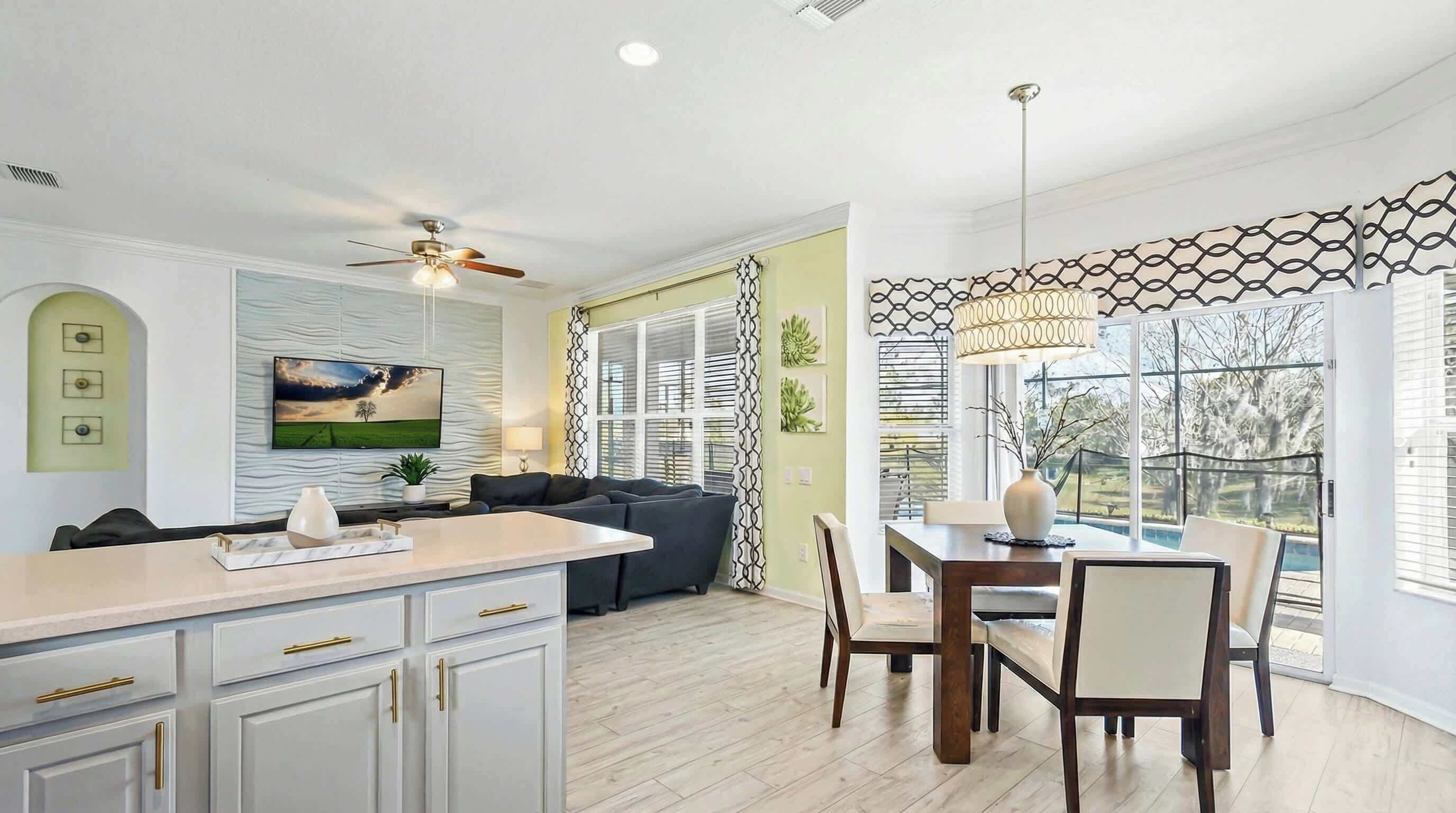 A modern kitchen with a dining area, a ceiling fan, and a large window with a view of the outdoors.