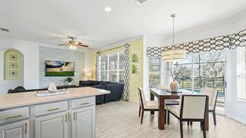 A modern kitchen with a dining area, a ceiling fan, and a large window with a view of the outdoors.