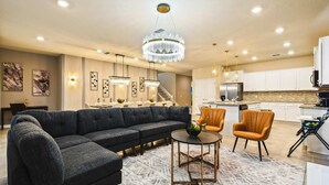 A modern living room with a sectional sofa, two armchairs, a coffee table, and a chandelier. - Mario Game Room Theater Loft w/ Pool Spa Disney (Davenport)