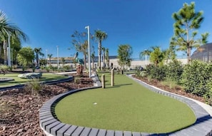 A miniature golf course with a green putting area, surrounded by landscaped gardens and palm trees.