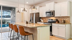 A modern kitchen with white cabinets, stainless steel appliances, a granite countertop, and a bar area with stools. - 5BR Windsor Island Resort w Private Pool Disney (Davenport)