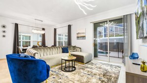 Un salon moderne comprenant un canapé, des fauteuils, une table basse et une grande fenêtre équipée de stores.