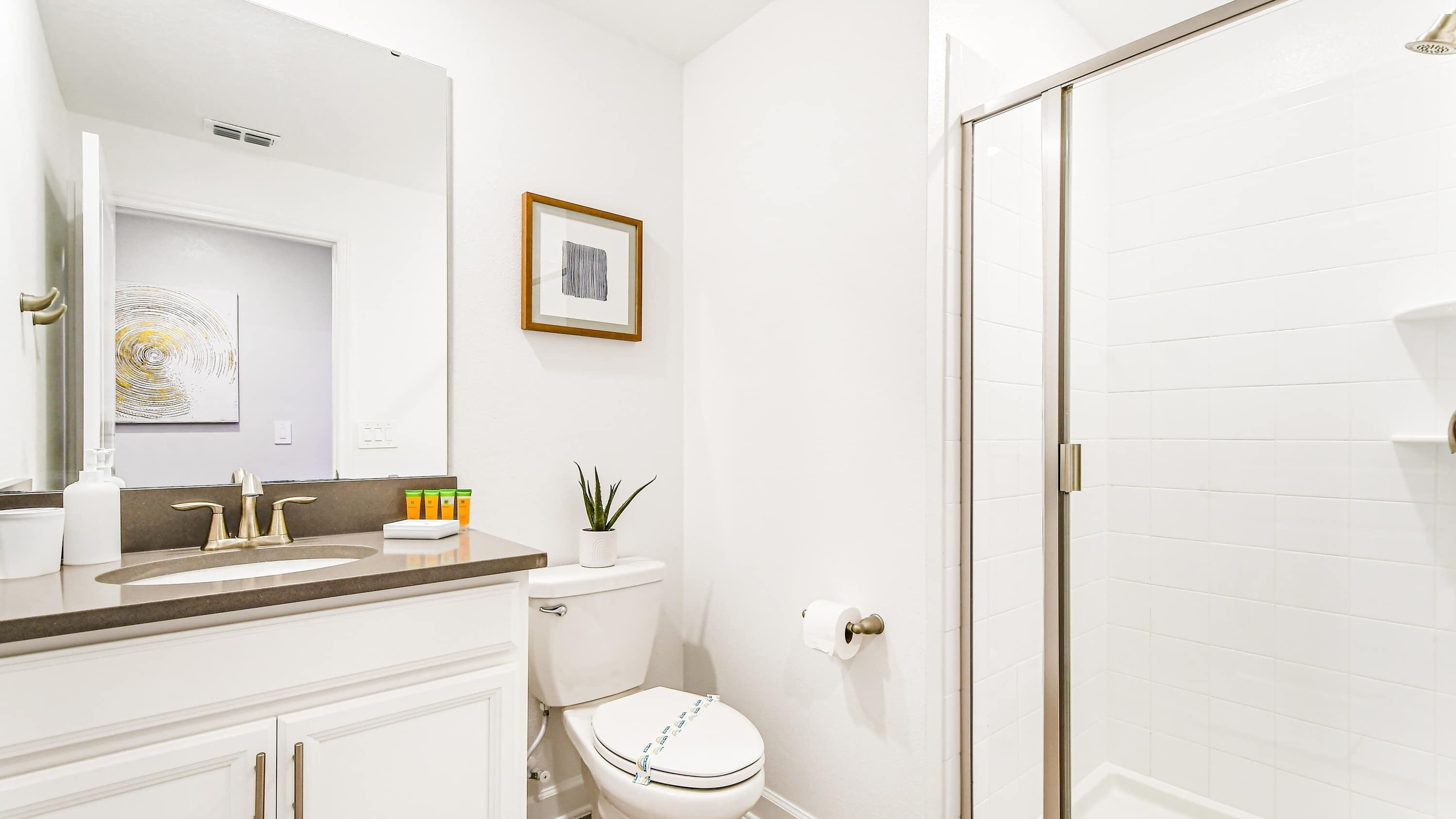 Un baño moderno con un lavamanos blanco, grifos dorados, un inodoro y una zona de ducha.