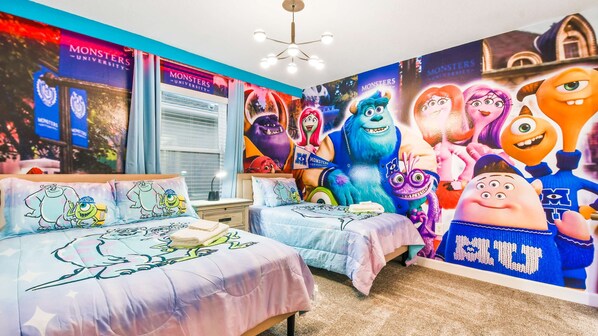 A bedroom with two beds, each with a Monsters University themed bedspread. The room features a large wall mural of Monsters University characters and a window with blinds.