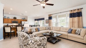 A living room with a sofa, coffee table, and patterned armchair. There is a kitchen area with wooden cabinets and a microwave. - Firework View 6BR Home Pool/spa/game Near Disney! (Kissimmee)