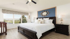 A bedroom with a large bed, two bedside tables, a ceiling fan, a window with a view, and a decorative mirror. - Firework View 6BR Home Pool/spa/game Near Disney! (Kissimmee)