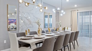 Uma sala de jantar moderna com uma mesa comprida posta para seis pessoas, cadeiras elegantes e um candelabro com várias luminárias.