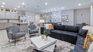 Uma sala de estar moderna com um sofá cinzento, duas poltronas, uma mesa de centro e um tapete com padrão marmorizado.