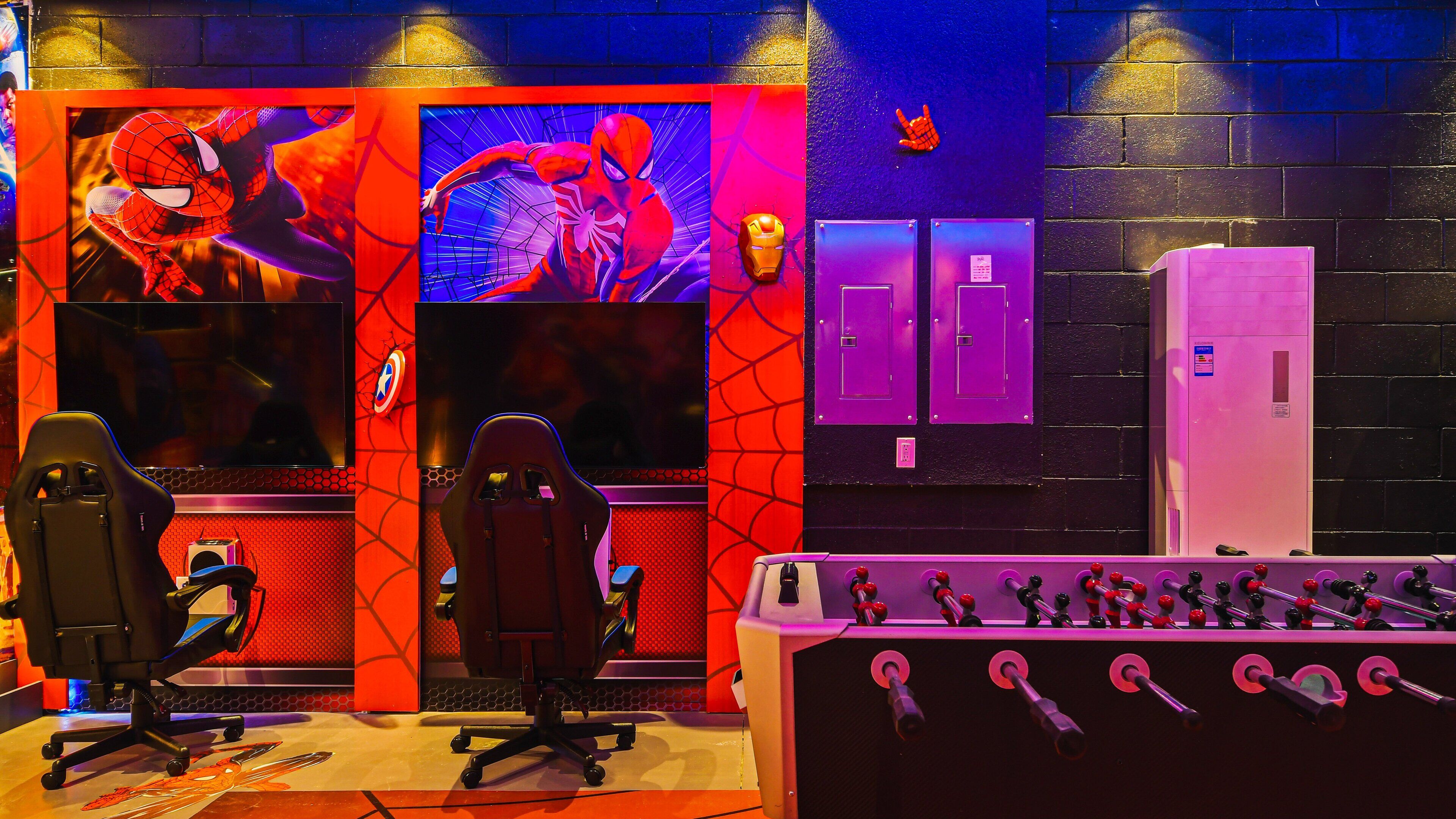A gaming room with two gaming chairs, a foosball table, and Spider-Man themed decorations.
