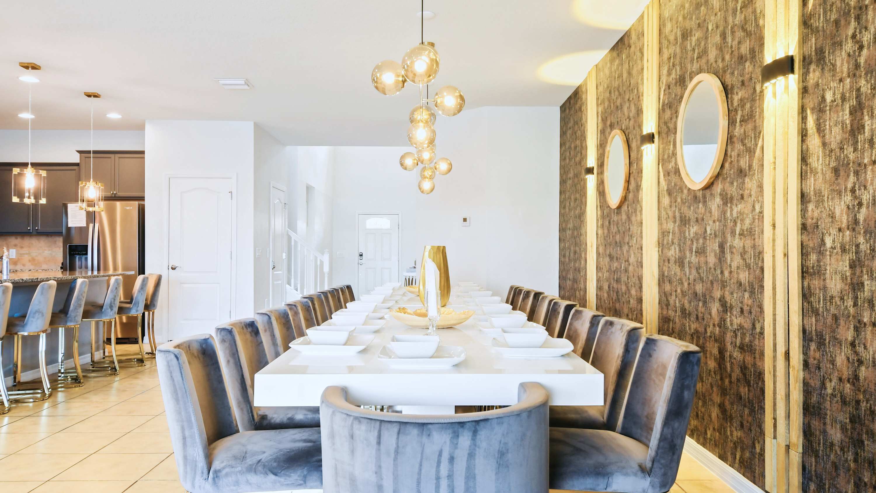 Une salle à manger moderne avec une longue table, des chaises à revêtement gris et un lustre.