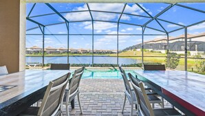 A covered outdoor dining area with a view of a lake and residential buildings. - Elegant Orlando Home: Pool, Spa & Theme Parks (Kissimmee)