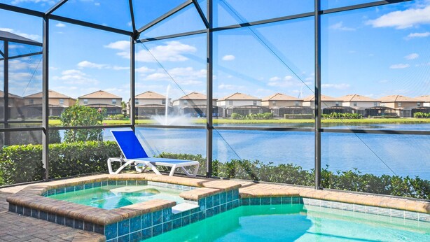 A pool area with a hot tub, a lounge chair, and a view of a lake and houses in the background. - Elegant Orlando Home: Pool, Spa & Theme Parks (Kissimmee)