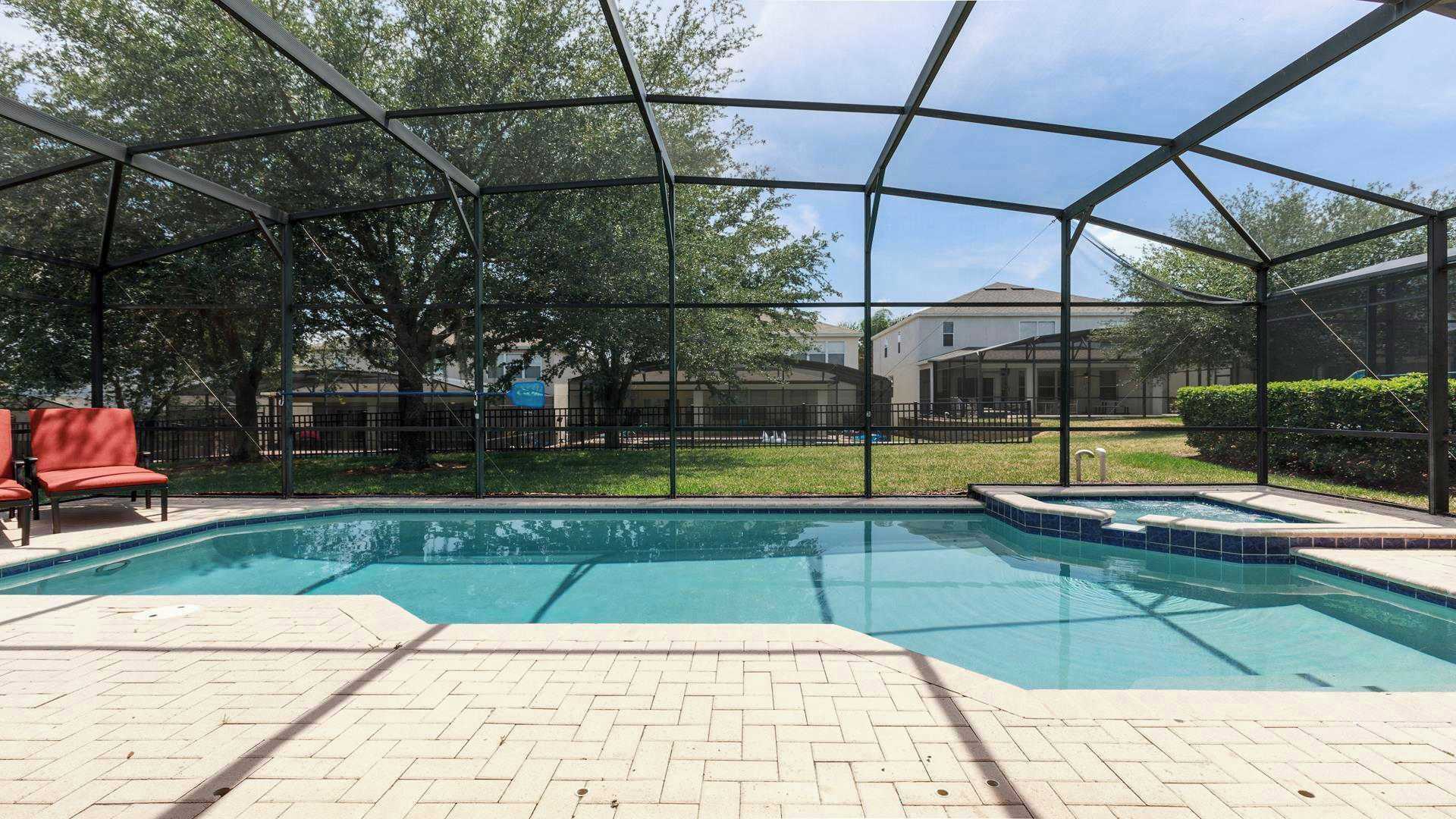 A covered outdoor swimming pool with a brick deck, surrounded by a metal fence and trees.