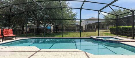 A covered outdoor swimming pool with a brick deck, surrounded by a metal fence and trees.