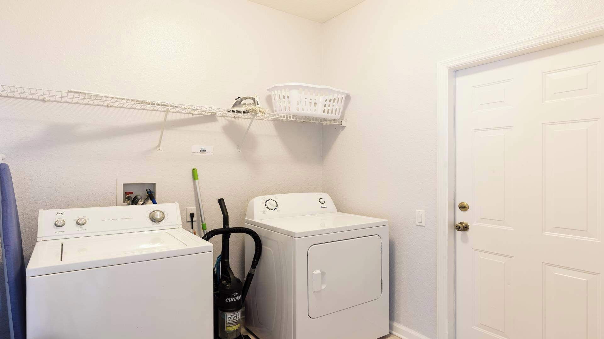 A laundry room with two stacked washers and dryers, a white basket on a shelf, and a door to the right.
