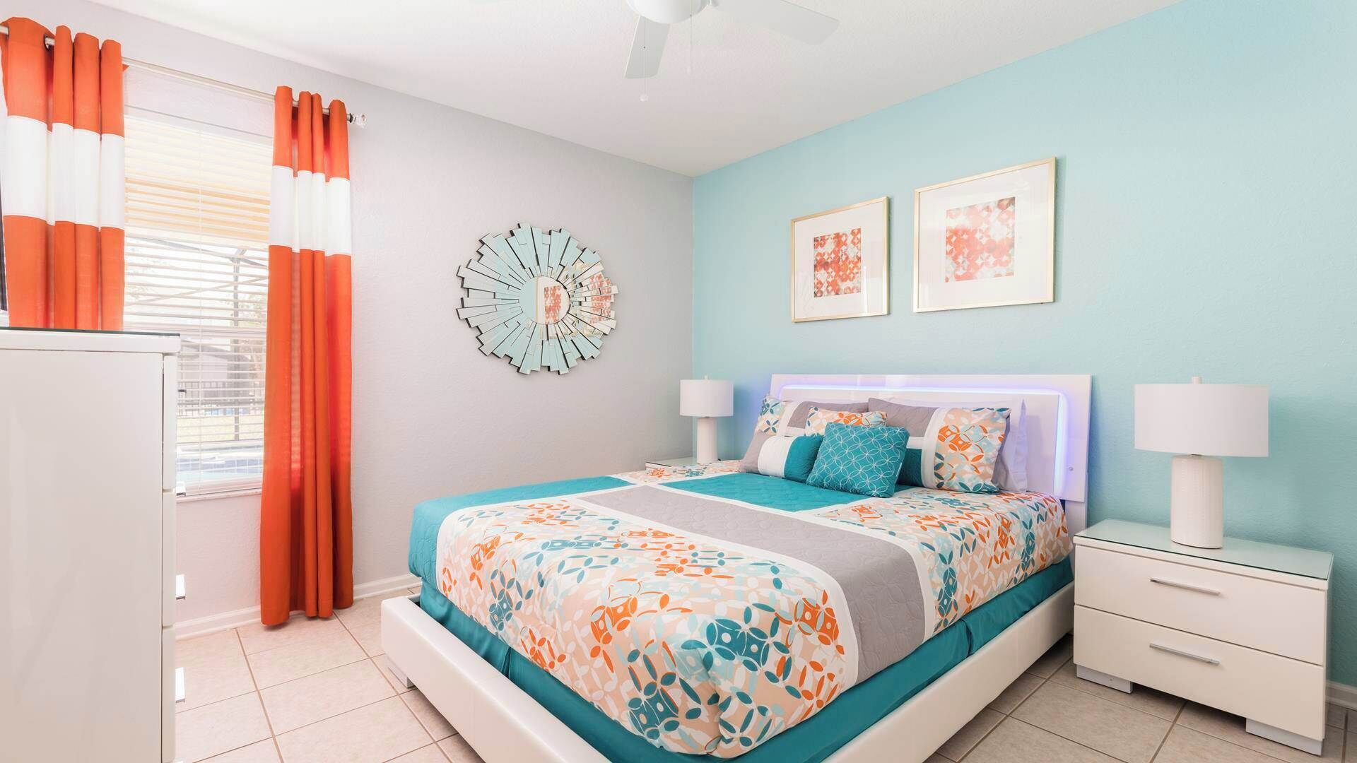A bedroom with a bed, two bedside tables, a wall clock, and two framed pictures.