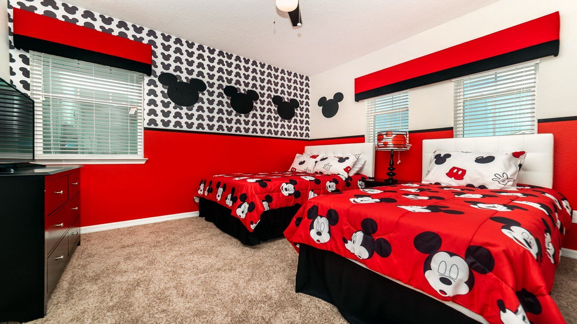 A bedroom with two beds, red and black bedding, a wall with Mickey Mouse patterns, and a red and black accent wall.