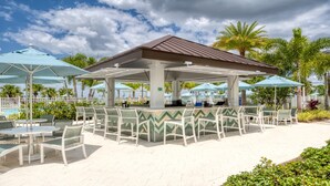 A covered outdoor seating area with tables and chairs, a pool in the background, and palm trees. - Disney Getaway: Pool, Spa, Games, Great Locale (Kissimmee)