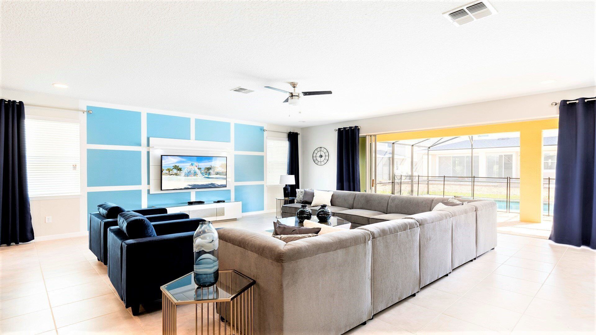 A modern living room with a large sectional sofa, a TV mounted on the wall, and a ceiling fan.
